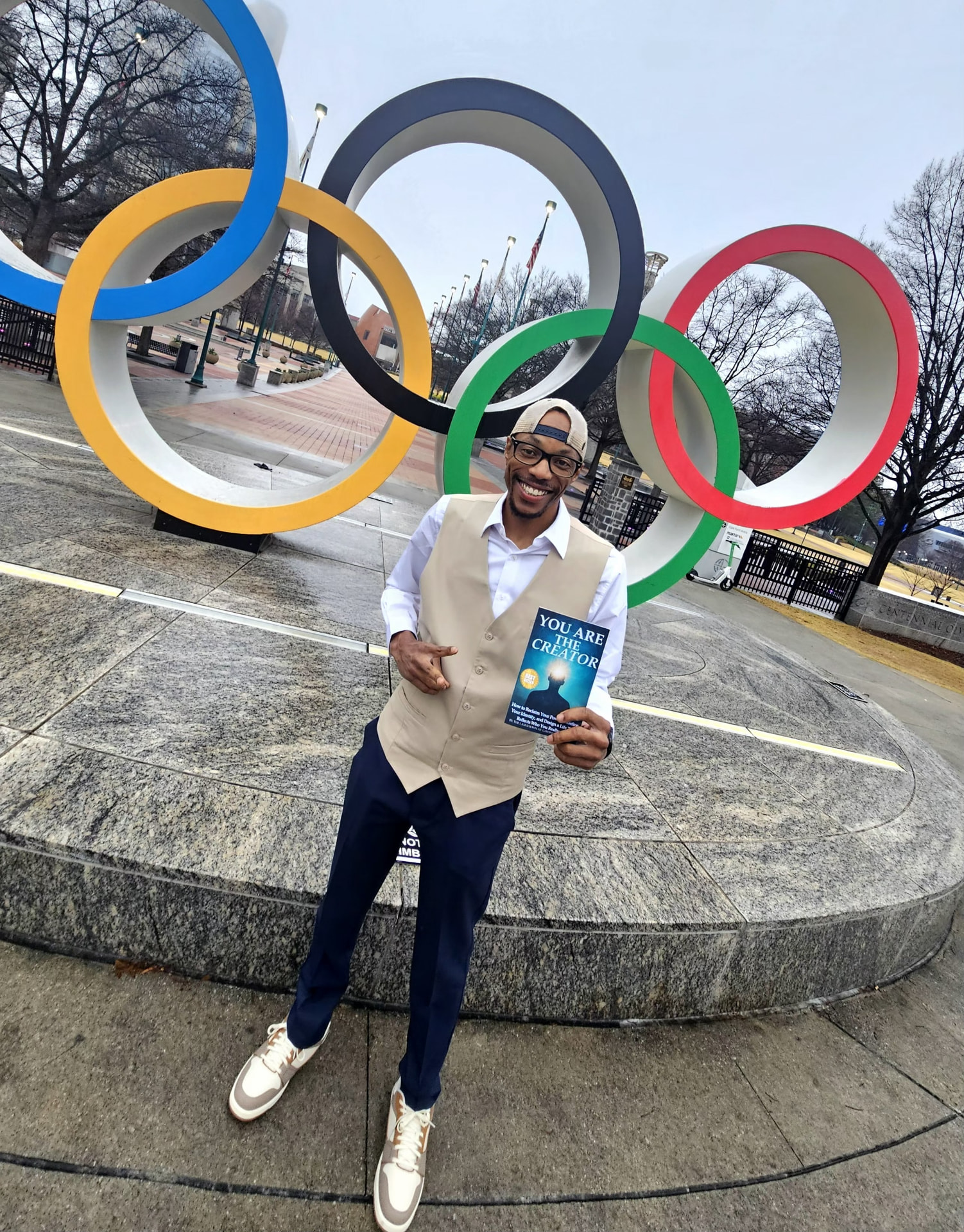 Geo Dixon holding his book You Are the Creator in front of the Atlanta Olympic Rings